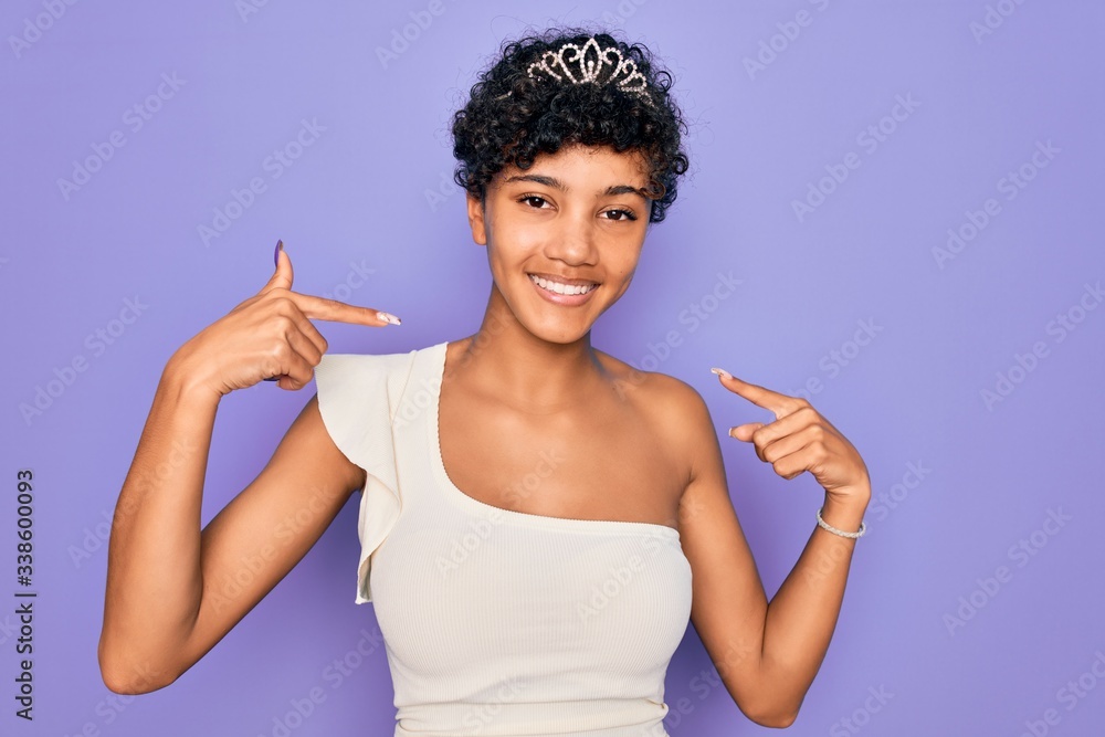 Young beautiful african american afro woman wearing tiara crown over purple background looking confident with smile on face, pointing oneself with fingers proud and happy. Young beautiful african american afro woman wearing tiara crown over purple background looking confident with smile on face, pointing oneself with fingers proud and happy.