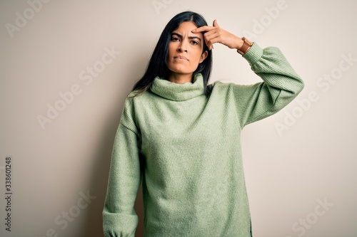 Young beautiful hispanic woman wearing green winter sweater over isolated background pointing unhappy to pimple on forehead, ugly infection of blackhead. Acne and skin problem © Krakenimages.com