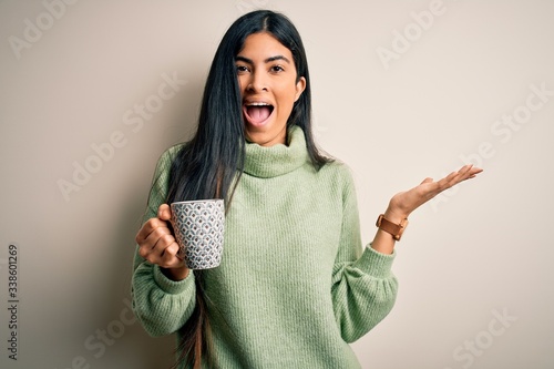 Young beautiful hispanic woman drinking a cup of hot coffee over isolated background very happy and excited, winner expression celebrating victory screaming with big smile and raised hands