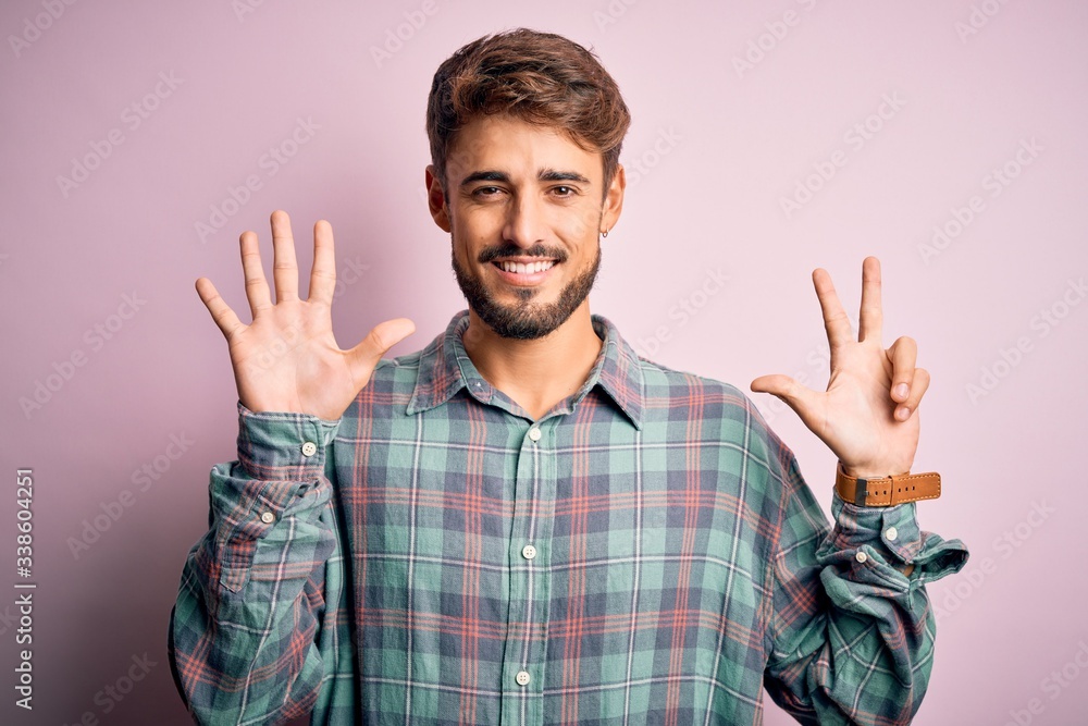 Young handsome man with beard wearing casual shirt standing over pink background showing and pointing up with fingers number eight while smiling confident and happy. Young handsome man with beard wearing casual shirt standing over pink background showing and pointing up with fingers number eight while smiling confident and happy.