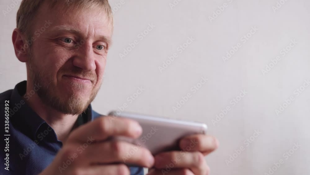 young man with a beard plays the game on his phone young man with a beard plays the game on his phone