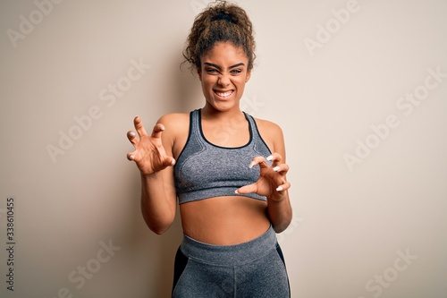 Young african american sportswoman doing sport wearing sportswear over white background smiling funny doing claw gesture as cat, aggressive and sexy expression © Krakenimages.com