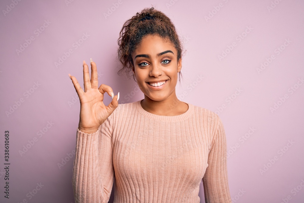 Young beautiful african american girl wearing casual sweater standing over pink background smiling positive doing ok sign with hand and fingers. Successful expression. Young beautiful african american girl wearing casual sweater standing over pink background smiling positive doing ok sign with hand and fingers. Successful expression.