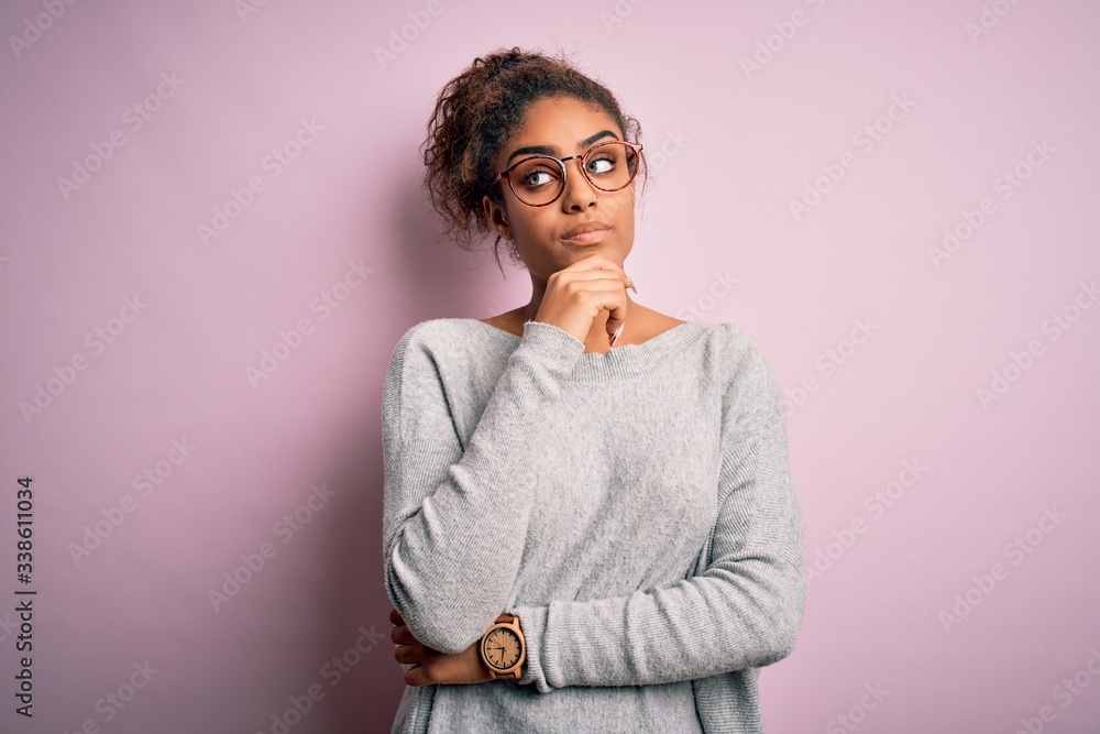 Young beautiful african american girl wearing sweater and glasses over pink background with hand on chin thinking about question, pensive expression. Smiling with thoughtful face. Doubt concept. Young beautiful african american girl wearing sweater and glasses over pink background with hand on chin thinking about question, pensive expression. Smiling with thoughtful face. Doubt concept.