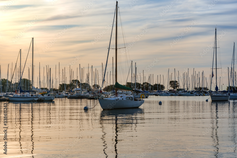 Sail boats docked in a marina, silhouetted against a colorful morning sky