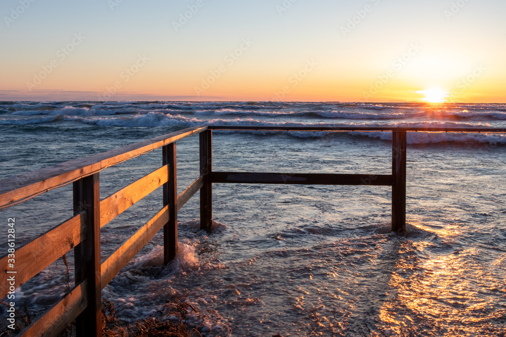Fototapeta premium sunset at Sauble Beach in early April. High water up to the fence.