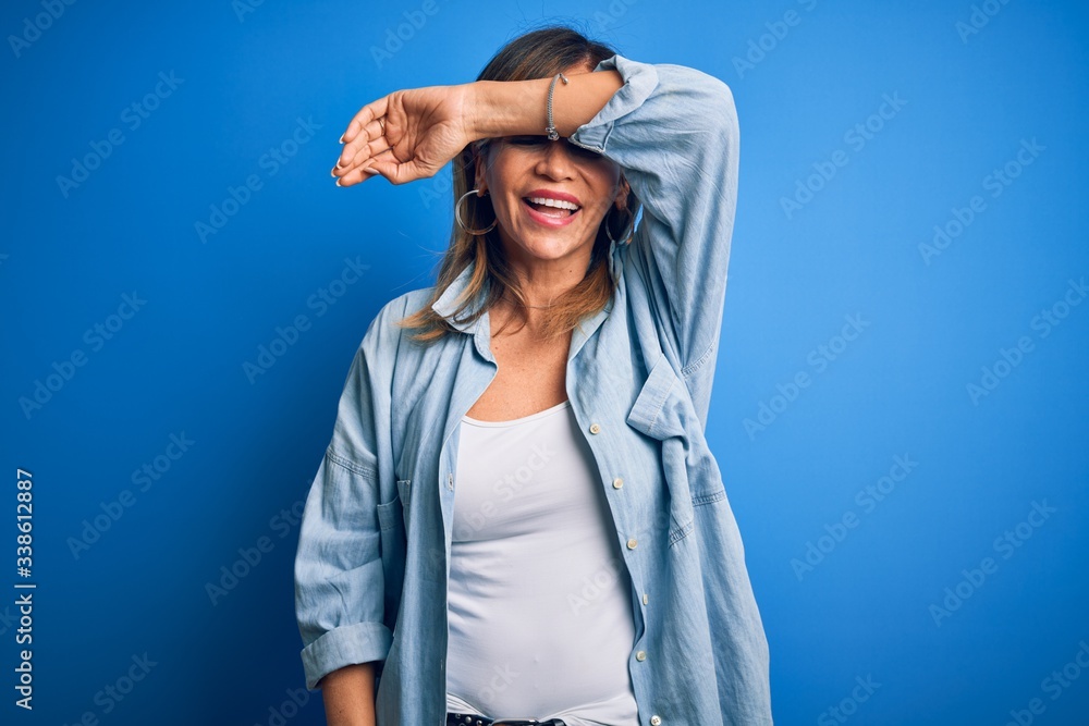 Middle age beautiful woman wearing casual shirt standing over isolated blue background covering eyes with arm smiling cheerful and funny. Blind concept. Middle age beautiful woman wearing casual shirt standing over isolated blue background covering eyes with arm smiling cheerful and funny. Blind concept.