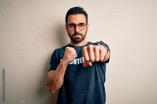 Handsome man with beard wearing t-shirt with volunteer message over white background Punching fist to fight, aggressive and angry attack, threat and violence