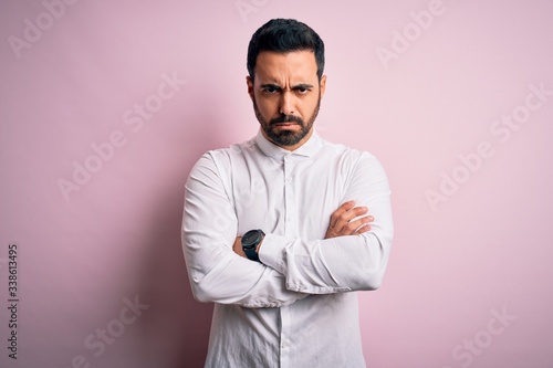 Young handsome man with beard wearing casual shirt standing over pink background skeptic and nervous, disapproving expression on face with crossed arms. Negative person.