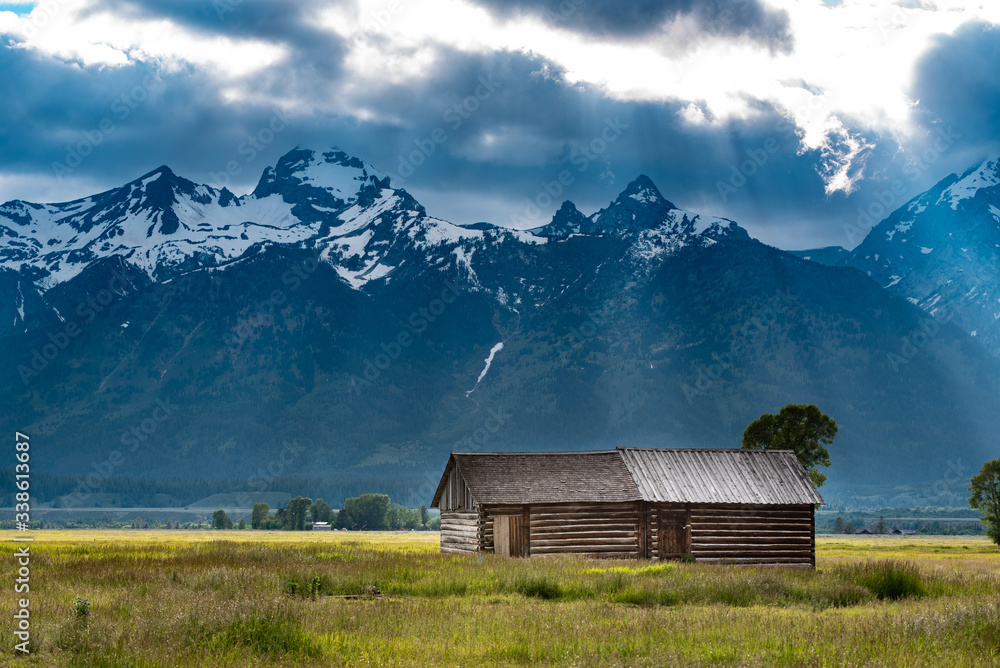 Rays breaking through storm clouds upon an old barn near the mountains in Mormon Row, Grand Teton National Park, Wyoming