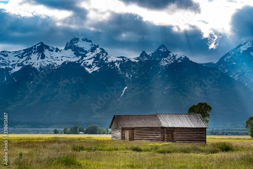 Rays breaking through storm clouds upon an old barn near the mountains in Mormon Row, Grand Teton National Park, Wyoming