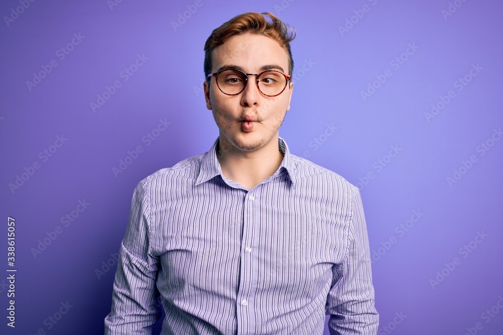 Young handsome redhead man wearing casual shirt and glasses over purple background making fish face with lips, crazy and comical gesture. Funny expression. Young handsome redhead man wearing casual shirt and glasses over purple background making fish face with lips, crazy and comical gesture. Funny expression.