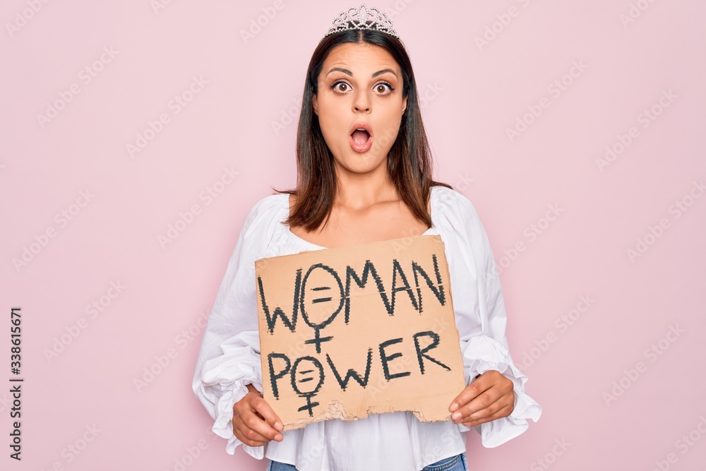 Girl wearing princess tiara asking for women rights holding banner with woman power message scared and amazed with open mouth for surprise, disbelief face Girl wearing princess tiara asking for women rights holding banner with woman power message scared and amazed with open mouth for surprise, disbelief face