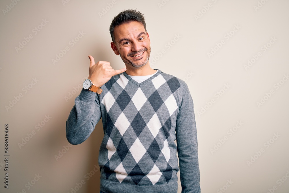 Young handsome man wearing casual sweater standing over isolated white background smiling doing phone gesture with hand and fingers like talking on the telephone. Communicating concepts. Young handsome man wearing casual sweater standing over isolated white background smiling doing phone gesture with hand and fingers like talking on the telephone. Communicating concepts.