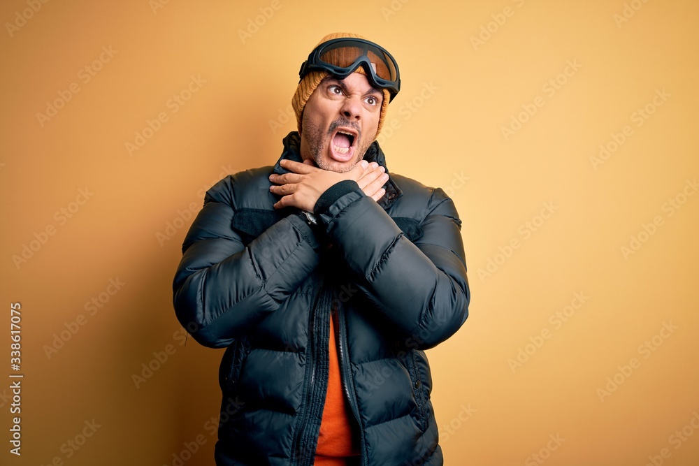 Young handsome skier man skiing wearing snow sportswear using ski goggles shouting suffocate because painful strangle. Health problem. Asphyxiate and suicide concept. Young handsome skier man skiing wearing snow sportswear using ski goggles shouting suffocate because painful strangle. Health problem. Asphyxiate and suicide concept.