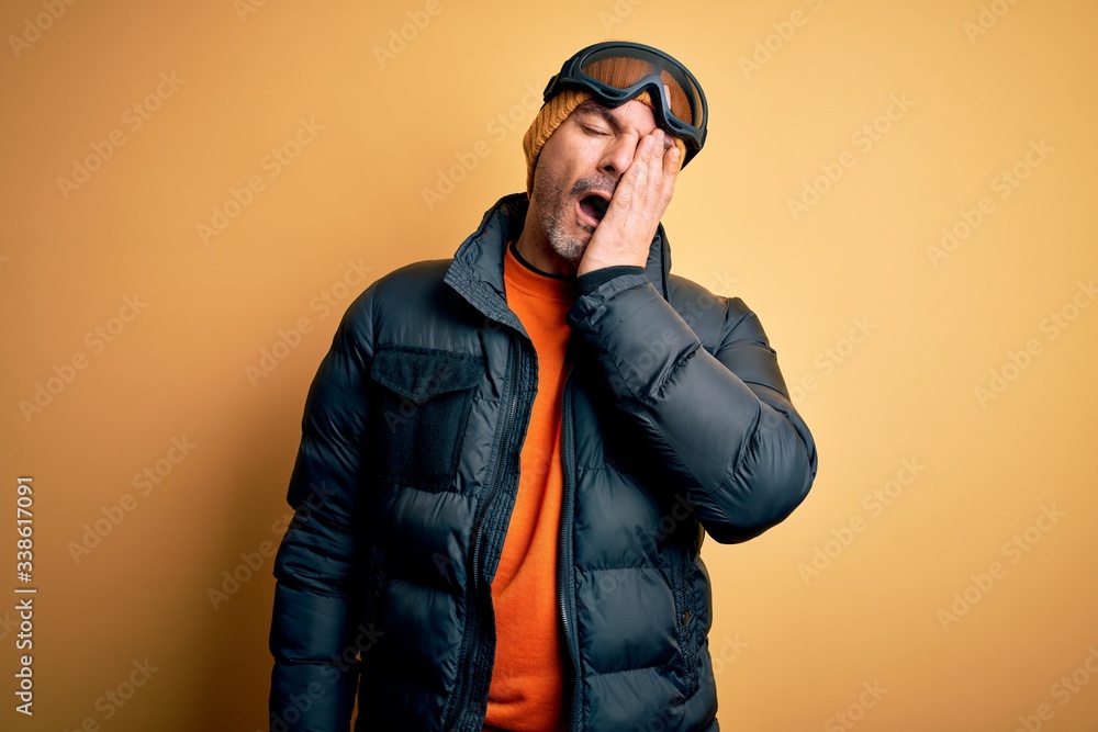 Young handsome skier man skiing wearing snow sportswear using ski goggles Yawning tired covering half face, eye and mouth with hand. Face hurts in pain. Young handsome skier man skiing wearing snow sportswear using ski goggles Yawning tired covering half face, eye and mouth with hand. Face hurts in pain.