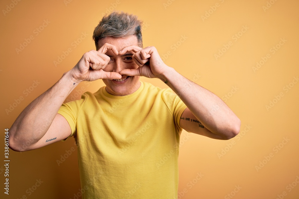 Young handsome modern man wearing yellow shirt over yellow isolated background Doing heart shape with hand and fingers smiling looking through sign Young handsome modern man wearing yellow shirt over yellow isolated background Doing heart shape with hand and fingers smiling looking through sign