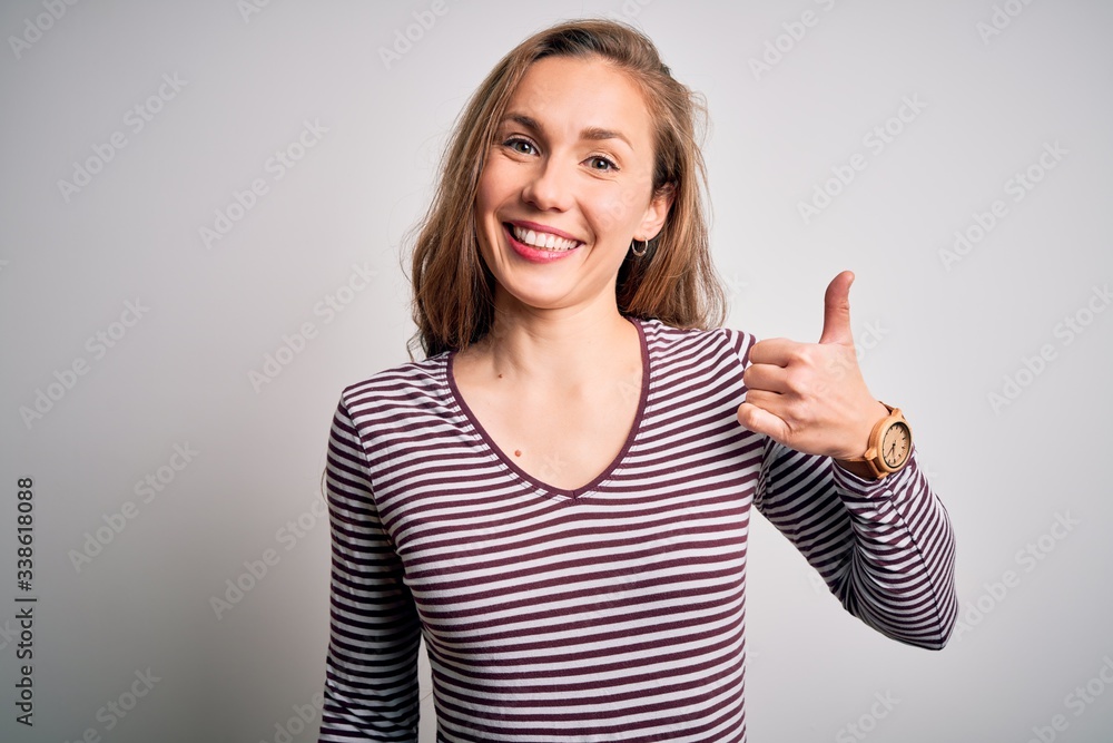 Young beautiful blonde woman wearing casual striped t-shirt over isolated white background doing happy thumbs up gesture with hand. Approving expression looking at the camera showing success. Young beautiful blonde woman wearing casual striped t-shirt over isolated white background doing happy thumbs up gesture with hand. Approving expression looking at the camera showing success.