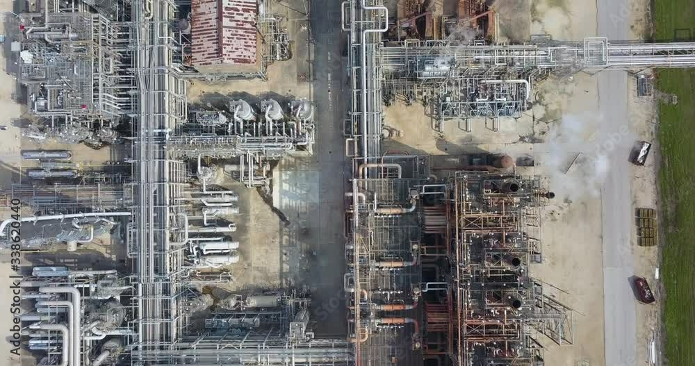 Bird's-eye view of the oil refinery. Oil refinery aerial view top down with complicated network of pipes. View of a chemical factory from above, white smoke come out of the cooling towers. Wide shot Bird's-eye view of the oil refinery. Oil refinery aerial view top down with complicated network of pipes. View of a chemical factory from above, white smoke come out of the cooling towers. Wide shot