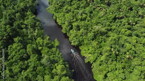 Tour boat on Rio Orinoco Delta, Venezuela lined by lush dense tropical rainforest, dark black waters aerial top down photo