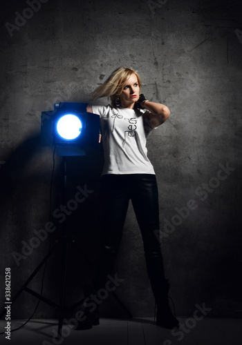 Young beautiful blond woman in stylish casual clothing and black boots standing near light fixture