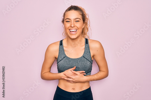 Young beautiful blonde sportswoman with blue eyes doing exercise wearing sportswear smiling and laughing hard out loud because funny crazy joke with hands on body.