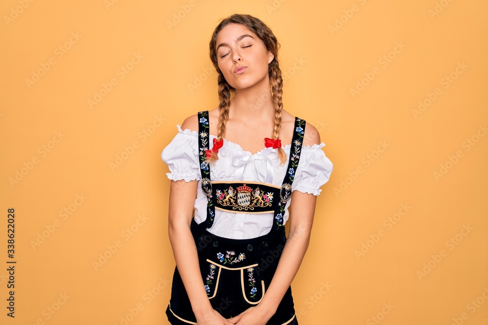 Young beautiful blonde german woman with blue eyes wearing traditional octoberfest dress looking at the camera blowing a kiss on air being lovely and sexy. Love expression. Young beautiful blonde german woman with blue eyes wearing traditional octoberfest dress looking at the camera blowing a kiss on air being lovely and sexy. Love expression.