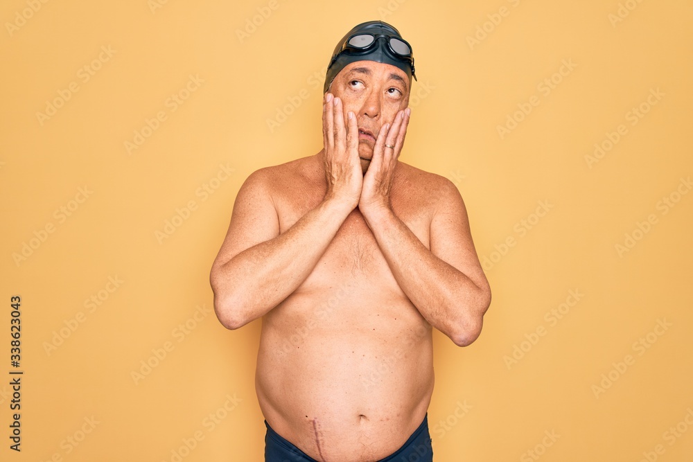 Middle age senior grey-haired swimmer man wearing swimsuit, cap and goggles Tired hands covering face, depression and sadness, upset and irritated for problem