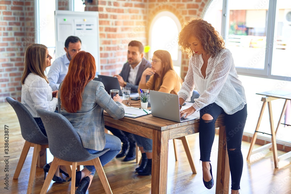 Group of business workers working together. Middle age beautiful businesswoman standing smiling happy looking at the camera at the office Group of business workers working together. Middle age beautiful businesswoman standing smiling happy looking at the camera at the office