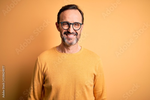 Middle age hoary man wearing casual sweater and glasses over isolated yellow background with a happy and cool smile on face. Lucky person. © Krakenimages.com