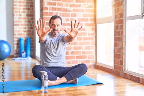 Middle age handsome sportman sitting on mat doing stretching yoga exercise at gym doing stop gesture with hands palms, angry and frustration expression