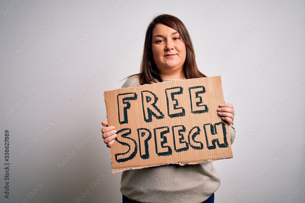 Beautiful plus size woman holding free speech banner for rights protest over isolated background with a confident expression on smart face thinking serious Beautiful plus size woman holding free speech banner for rights protest over isolated background with a confident expression on smart face thinking serious