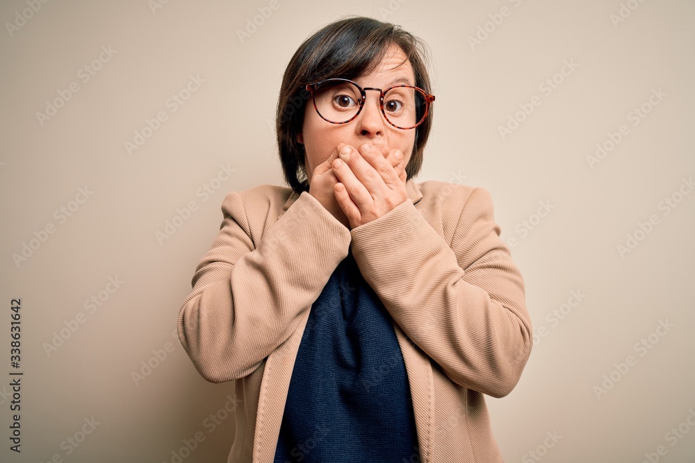 Young down syndrome business woman wearing glasses standing over isolated background shocked covering mouth with hands for mistake. Secret concept. Young down syndrome business woman wearing glasses standing over isolated background shocked covering mouth with hands for mistake. Secret concept.