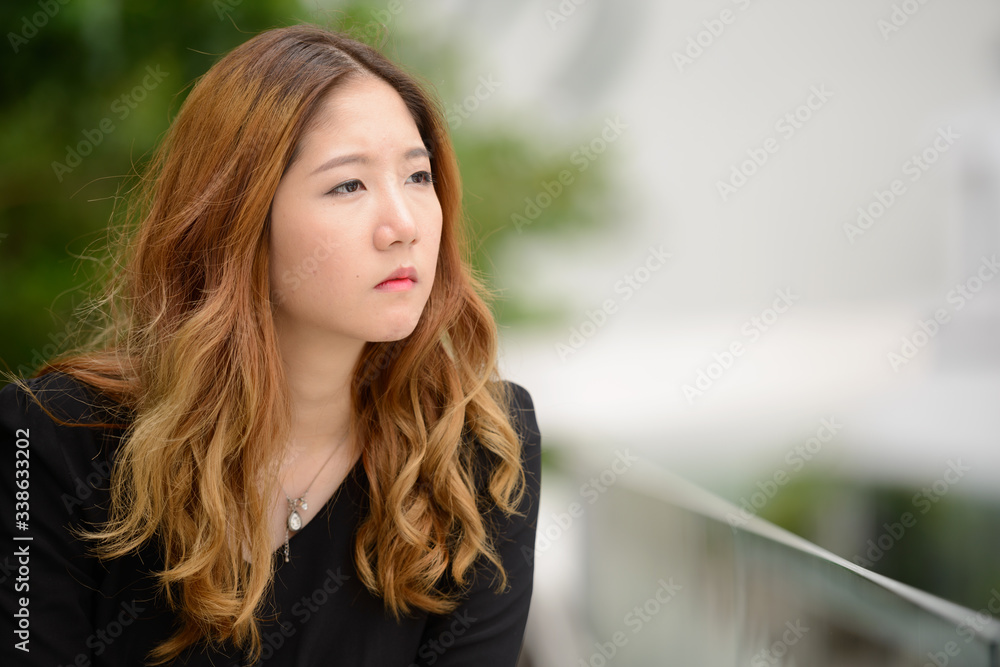 Obraz premium Young Asian businesswoman thinking and looking at view of the city