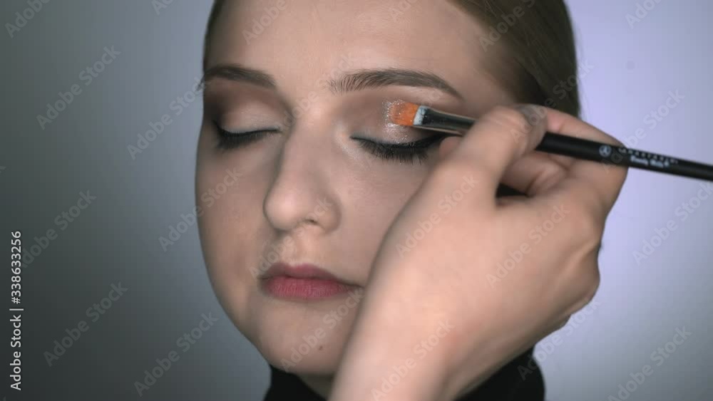 Makeup artist making professional make-up for young woman in beauty studio. Make up Artist uses brush to applies glitter on eyes Makeup artist making professional make-up for young woman in beauty studio. Make up Artist uses brush to applies glitter on eyes
