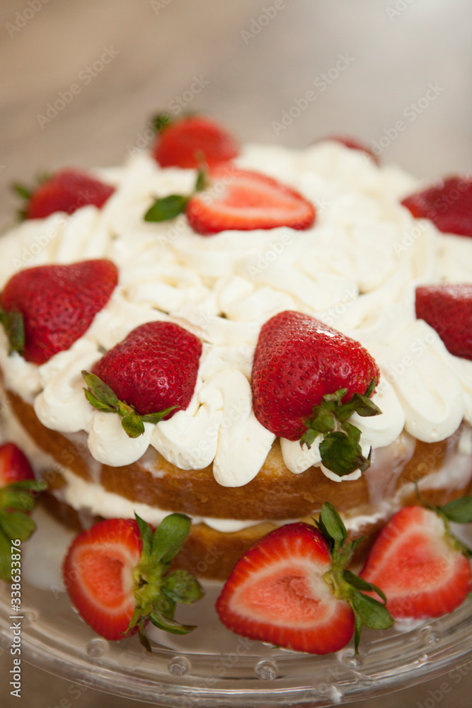 Two layer cake with strawberries and whipped cream on a glass cake platter Two layer cake with strawberries and whipped cream on a glass cake platter