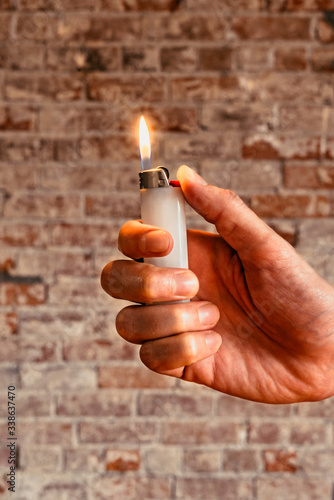 Male hand holding a white lighter with a flame ignited bright