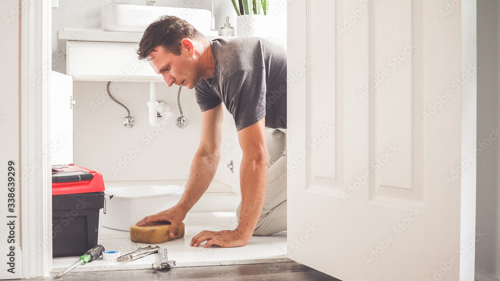 Man At Home Mopping Up Water From Leaking Pipe in Bathroom Man At Home Mopping Up Water From Leaking Pipe in Bathroom
