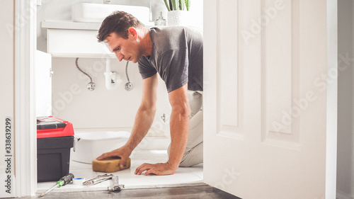 Man At Home Mopping Up Water From Leaking Pipe in Bathroom