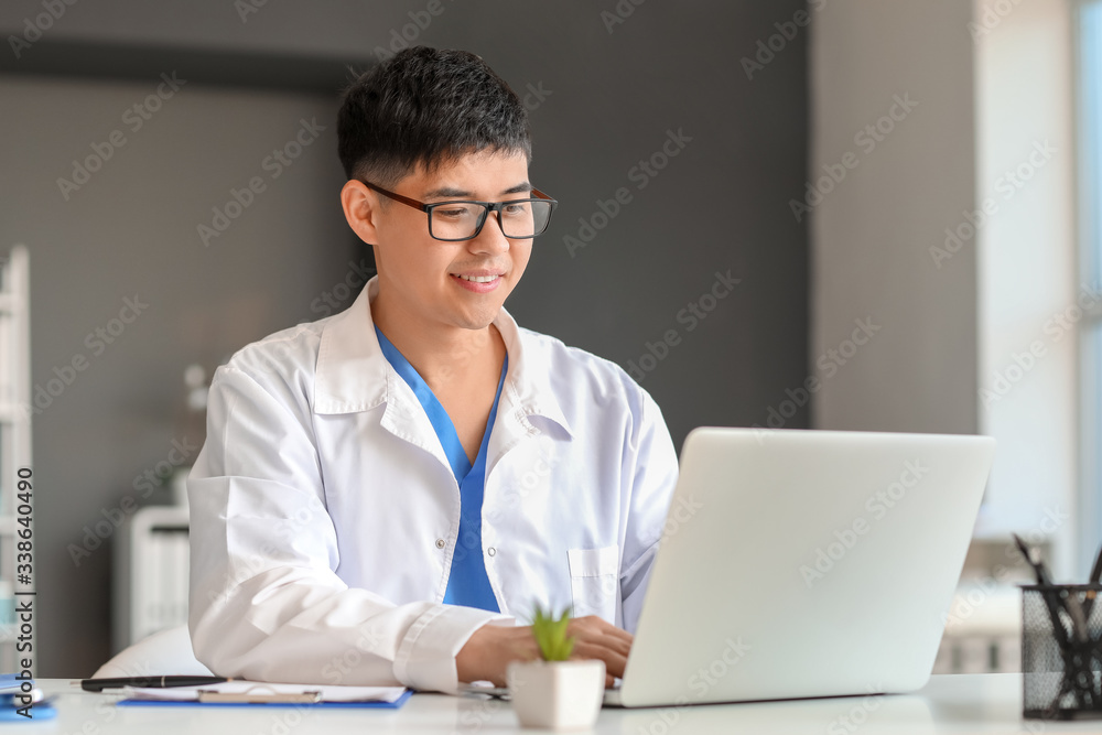 Male Asian doctor working on laptop in clinic Male Asian doctor working on laptop in clinic