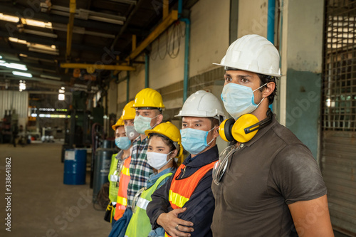 Team engineers and technician wearing protective mask to Protect Against Covid-19 standing at factory. © visoot