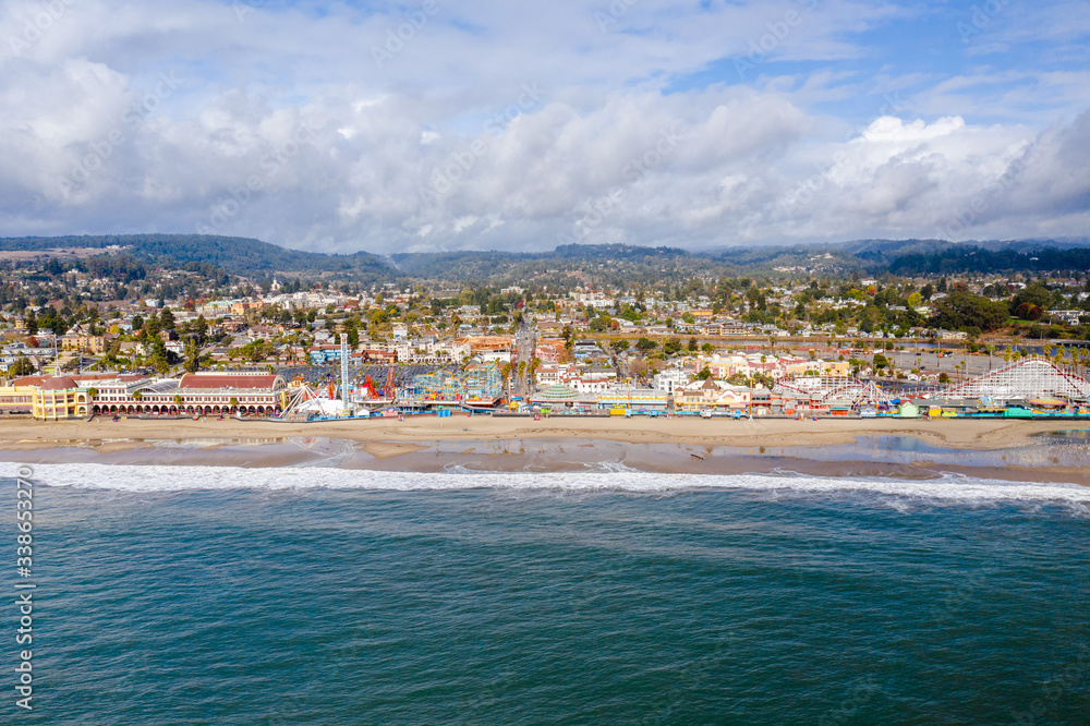Aerial drone shot of Santa Cruz Beach Boardwalk. The colorful amusement park is next to the beach with mountains in the background. 