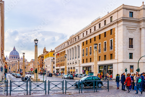 Rome, Italy. People/ Tourists, vehicles/ cars, bikes/ motorbikes in Saint Peters Square in Vatican City. The Basilica Cathedral, dome shape building with cross on top, in background © Debbie Ann Powell