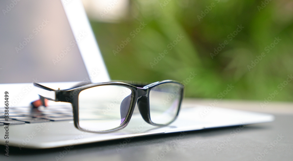 Spectacles on top of computer laptop with home and green nature background. Copy space.