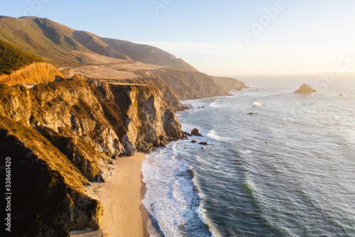 Aerial drone view of the Big Sur coastline in California. Beautiful golden light hitting the side of the cliffs at sunset along the coastal road. 