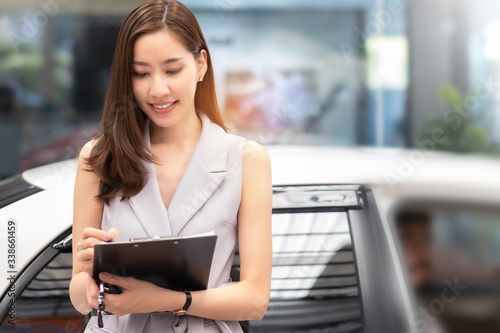 Salesperson working at car dealership.Young Asian woman  consultant and couple buyers signing contract for new car in auto show. Concept for car rental or sale.