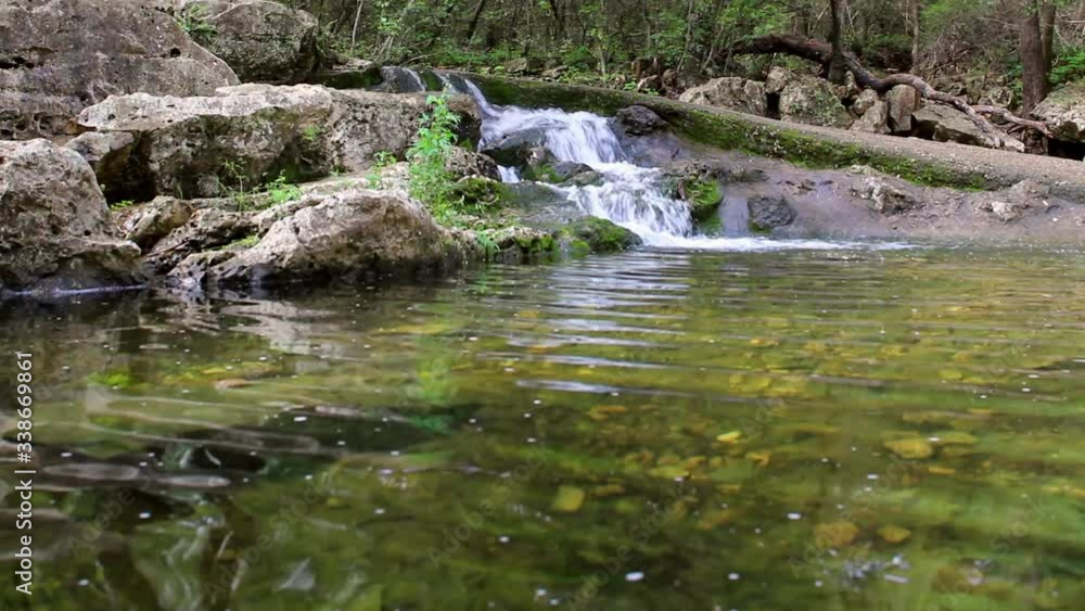 Creek waterfall flowing into a large pool below. Waterfall is shaped by concrete walking path above that seamlessly blends into the surroundings. Lot of moss by falls and trees in the background. Creek waterfall flowing into a large pool below. Waterfall is shaped by concrete walking path above that seamlessly blends into the surroundings. Lot of moss by falls and trees in the background.