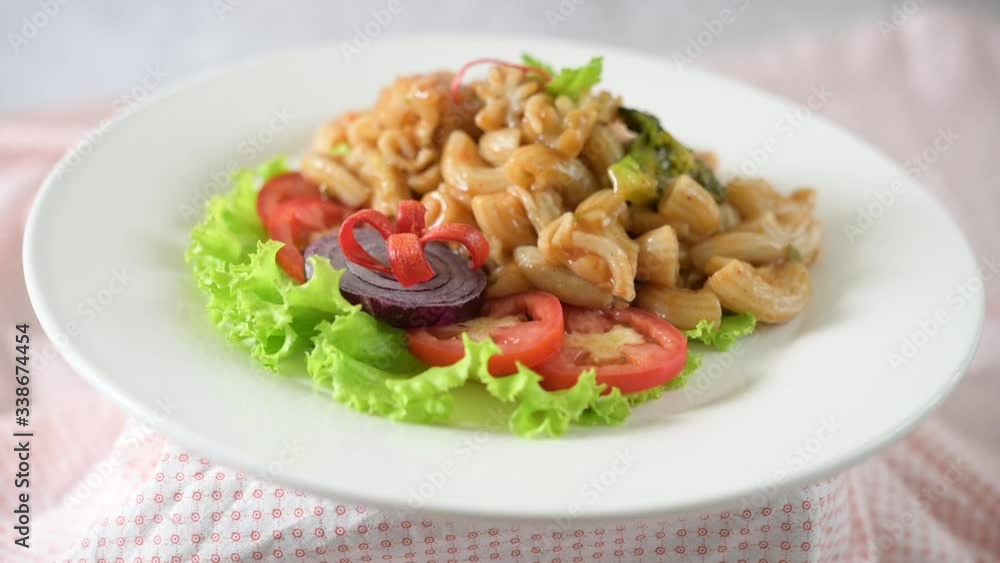 Stir fried macaroni with shrimp, squid, tomatoes, peppers and broccoli on a white plate Stir fried macaroni with shrimp, squid, tomatoes, peppers and broccoli on a white plate
