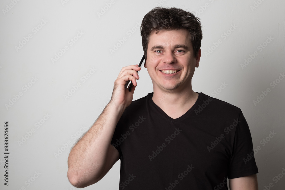 Man is talking on a cell phone. Smiling young man in a black T-shirt talking on the phone. Man is talking on a cell phone. Smiling young man in a black T-shirt talking on the phone.