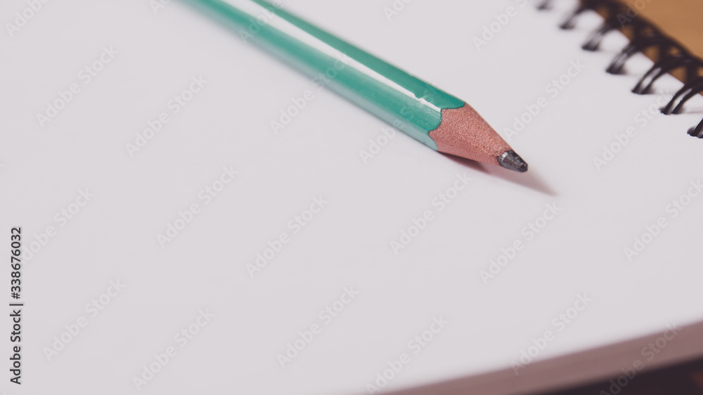 Closeup of a green pencil on a notebook. Notepad open on a blank page on the table. Closeup of a green pencil on a notebook. Notepad open on a blank page on the table.